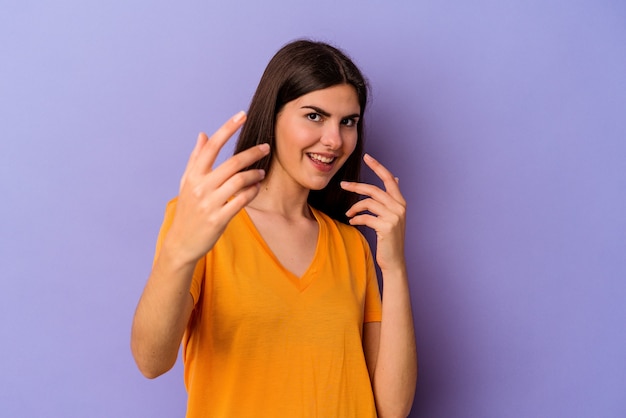 Junge kaukasische Frau, die auf violettem Hintergrund isoliert ist und mit dem Finger auf Sie zeigt, als ob sie einladen würde, näher zu kommen.