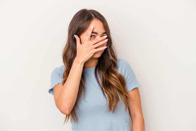 Junge kaukasische Frau, die auf weißem Hintergrund isoliert ist, blinzelt durch die Finger in die Kamera, verlegen, das Gesicht zu bedecken.