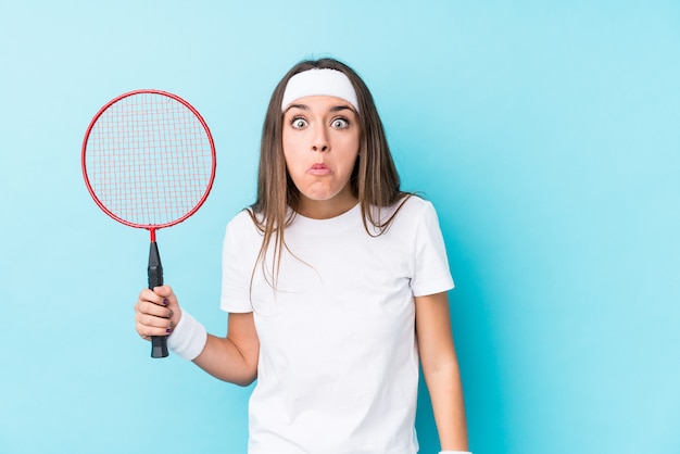 Junge kaukasische Frau, die Badminton spielt, zuckte isoliert mit den Schultern und offenen Augen verwirrt.