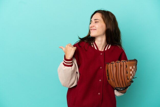 Junge kaukasische Frau, die Baseball spielt, isoliert auf blauem Hintergrund, der auf die Seite zeigt, um ein Produkt zu präsentieren