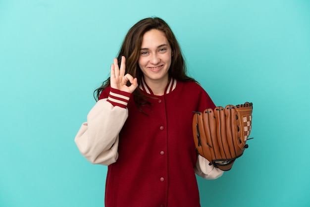 Junge kaukasische Frau, die Baseball spielt, isoliert auf blauem Hintergrund, der ein OK-Zeichen mit den Fingern zeigt