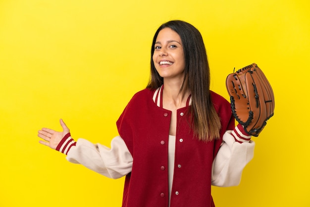 Junge kaukasische Frau, die Baseball spielt, isoliert auf gelbem Hintergrund, der die Hände zur Seite ausstreckt, um einzuladen, zu kommen