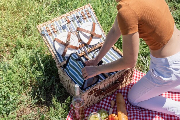 Junge kaukasische Frau, die draußen Picknickkorb vorbereitet, bereit, ein Picknick zu haben