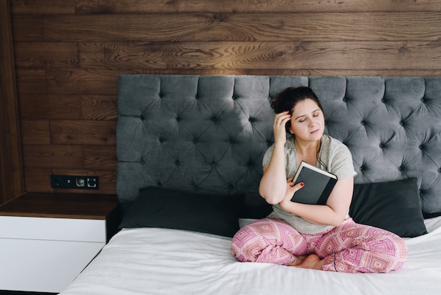 Junge kaukasische Frau, die ein Buch auf ihrem Bett in ihrem Schlafzimmer liest, das bequem ist