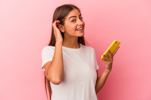 Junge kaukasische Frau, die ein Mobiltelefon isoliert auf rosa Wand hält und versucht, einen Klatsch zu hören.