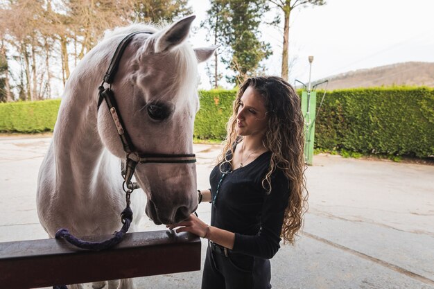 Junge kaukasische Frau, die ein weißes Pferd für eine Fahrt vorbereitet