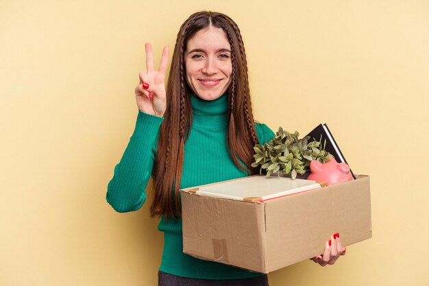 Junge kaukasische Frau, die eine Bewegung auf gelbem Hintergrund macht, die Nummer zwei mit den Fingern zeigt.