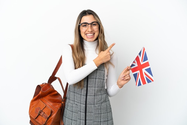 Junge kaukasische Frau, die eine britische Flagge isoliert auf weißem Hintergrund hält und auf die Seite zeigt, um ein Produkt zu präsentieren