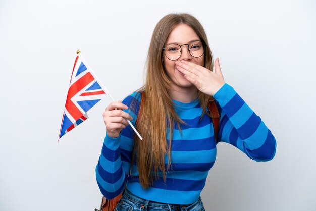 Junge kaukasische Frau, die eine britische Flagge lokalisiert auf weißem Hintergrund glücklich und lächelnd bedeckt Mund mit Hand hält