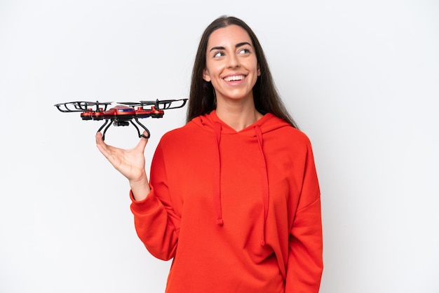 Junge kaukasische Frau, die eine Drohne isoliert auf weißem Hintergrund hält und eine Idee denkt, während sie nach oben schaut