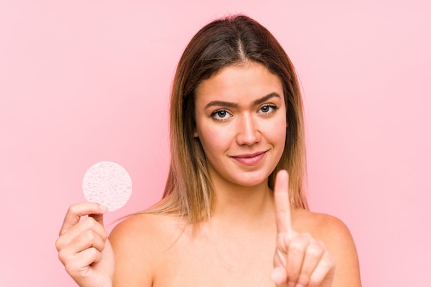 Junge kaukasische Frau, die eine Gesichtsscheibe lokalisiert hält, Nummer Eins mit dem Finger zeigend.