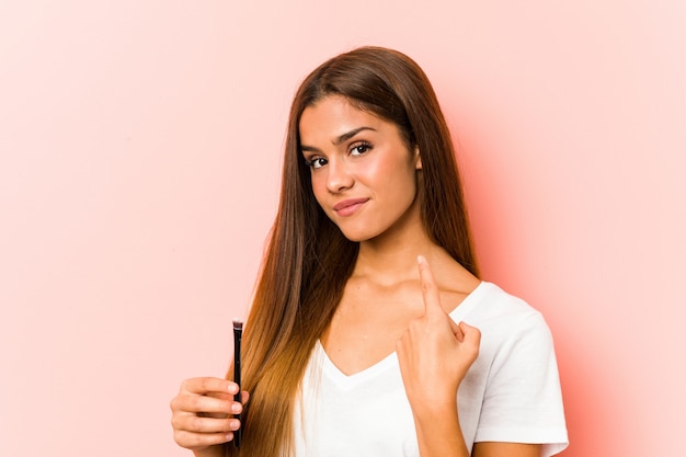 Junge kaukasische Frau, die eine Hautbürste hält, die mit dem Finger auf Sie zeigt, als ob die Einladung näher kommt