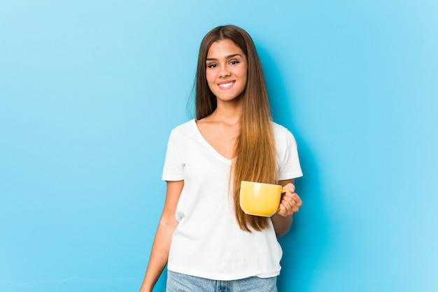 Junge kaukasische Frau, die eine Kaffeetasse glücklich, lächelnd und nett hält.