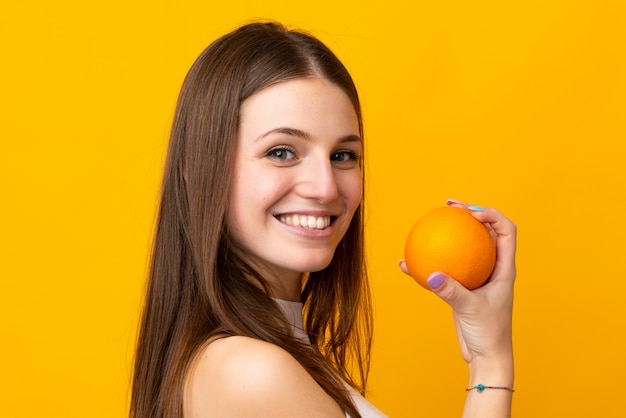 Junge kaukasische Frau, die eine Orange auf orange Wand hält