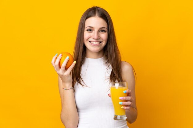 Junge kaukasische Frau, die eine Orange auf orange Wand hält