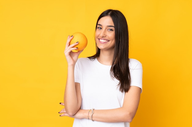 Junge kaukasische Frau, die eine Orange lokalisiert auf Gelb hält