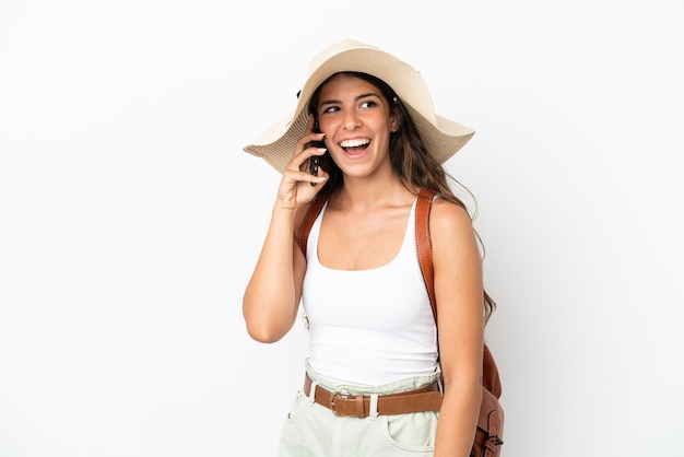 Junge kaukasische Frau, die eine Pamela in den Sommerferien trägt, isoliert auf weißem Hintergrund, die ein Gespräch mit dem Mobiltelefon führt