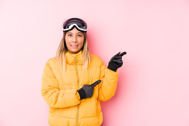 Junge kaukasische Frau, die eine Skikleidung in einem rosa schockierten Zeigen mit Zeigefingern auf einen Kopienraum trägt.