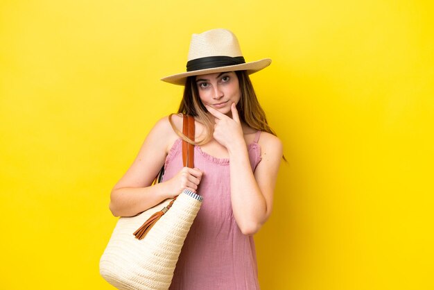 Junge kaukasische Frau, die eine Strandtasche hält, die auf gelbem Hintergrunddenken isoliert ist