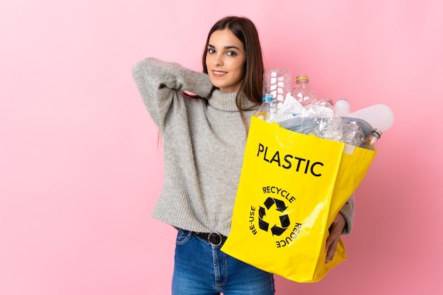 Junge kaukasische Frau, die eine Tasche voller Plastikflaschen hält, um lokalisiert auf rosa Lachen zu recyceln