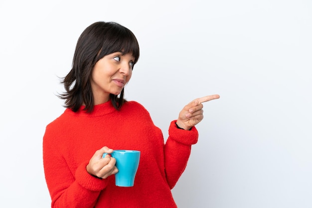 Junge kaukasische Frau, die eine Tasse Kaffee isoliert auf weißem Hintergrund hält, mit dem Finger zur Seite zeigt und ein Produkt präsentiert