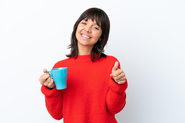 Junge kaukasische Frau, die eine Tasse Kaffee isoliert auf weißem Hintergrund mit Daumen nach oben hält, weil etwas Gutes passiert ist