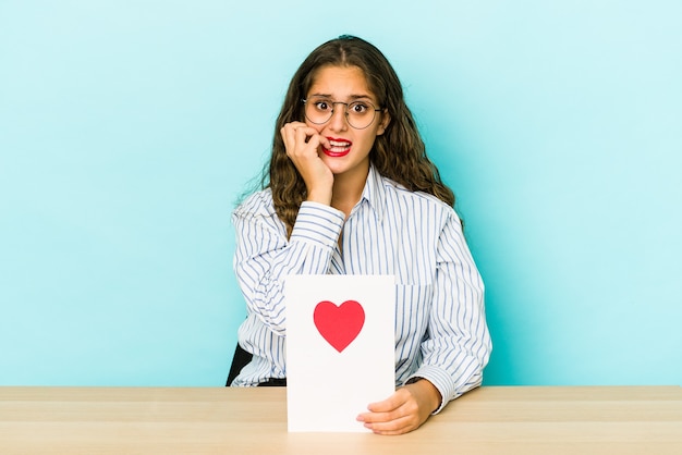 Junge kaukasische Frau, die eine Valentinstagkarte hält, isolierte beißende Fingernägel, nervös und sehr ängstlich.