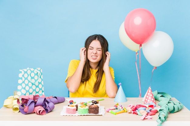 Junge kaukasische Frau, die einen Geburtstag organisiert, der Ohren mit Händen bedeckt.