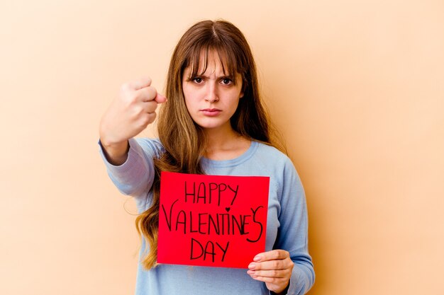 Junge kaukasische Frau, die einen glücklichen Valentinstag lokalisiert zeigt, zeigt Faust, aggressiven Gesichtsausdruck.