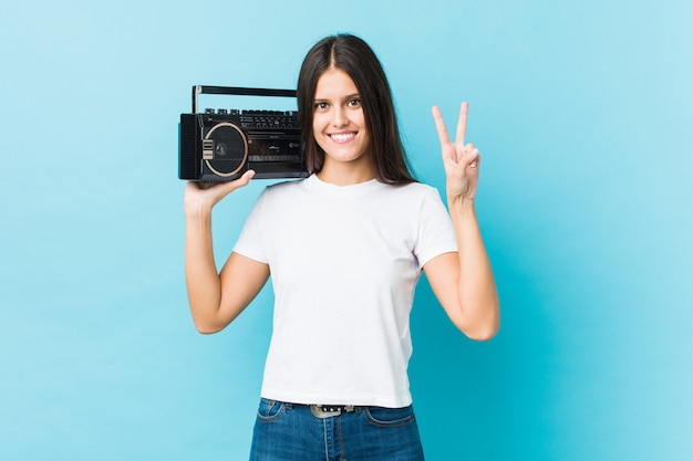 Junge kaukasische Frau, die einen Guettoblaster zeigt Nummer zwei mit den Fingern hält.