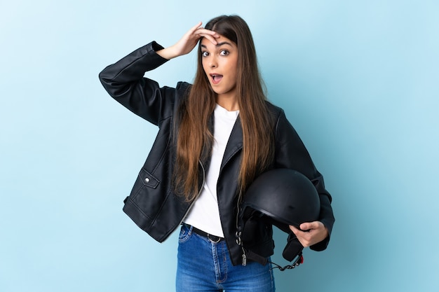 Junge kaukasische Frau, die einen Motorradhelm lokalisiert auf Blau tut, der Überraschungsgeste tut, während zur Seite schaut