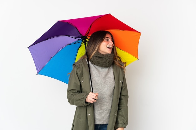 Junge kaukasische Frau, die einen Regenschirm lokalisiert auf weißem Lachen in seitlicher Position hält