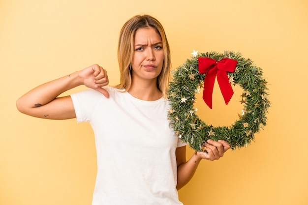 Junge kaukasische Frau, die einen Weihnachtskranz einzeln auf gelbem Hintergrund hält, fühlt sich stolz und selbstbewusst, Beispiel zu folgen.