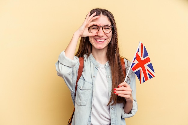 Junge kaukasische Frau, die Englisch isoliert auf gelbem Hintergrund lernt, aufgeregt, die Geste auf dem Auge zu halten.