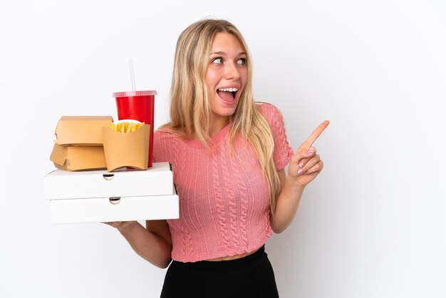 Junge kaukasische Frau, die fettes Essen isoliert auf blauem Hintergrund hält und beabsichtigt, die Lösung zu realisieren, während sie einen Finger hochhebt