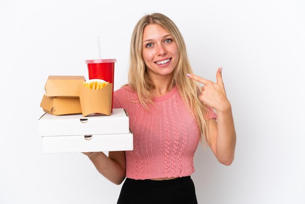 Junge kaukasische Frau, die fettes Essen isoliert auf blauem Hintergrund hält und eine Daumen-nach-oben-Geste gibt