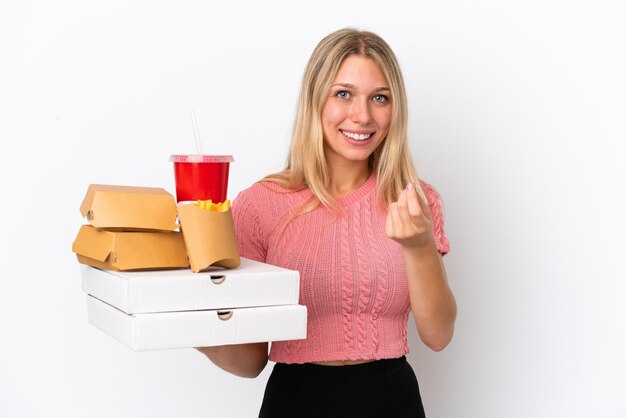 Junge kaukasische Frau, die fettes Essen isoliert auf blauem Hintergrund hält und Geldgeste macht