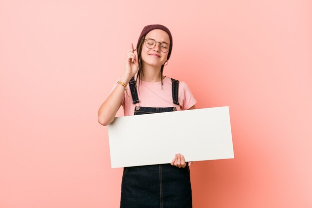 Junge kaukasische Frau, die Finger einer Plakatüberfahrt für das Haben des Glücks hält