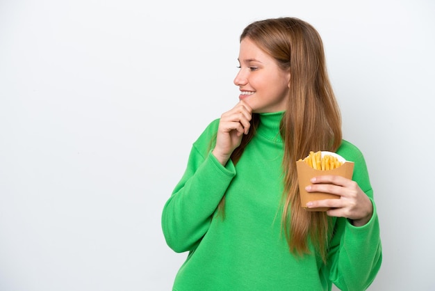 Junge kaukasische Frau, die gebratene Chips lokalisiert auf weißem Hintergrund hält, eine Idee denkend und Seite schauend