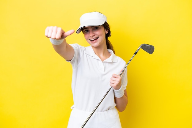 Junge kaukasische Frau, die Golf spielt, isoliert auf gelbem Hintergrund, mit einer Daumen-nach-oben-Geste