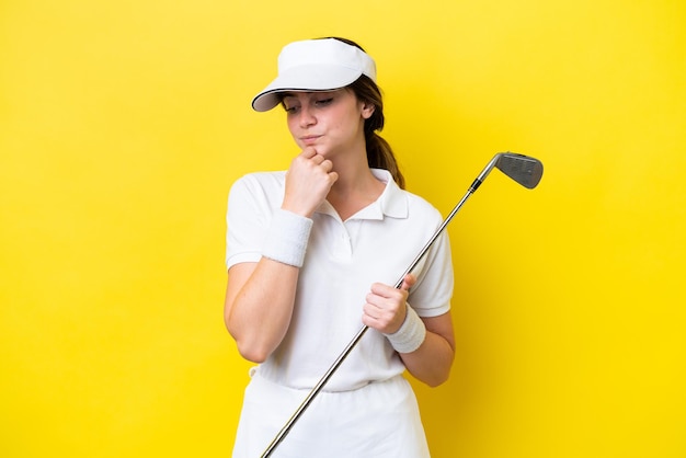 Junge kaukasische Frau, die Golf spielt, isoliert auf gelbem Hintergrund und Zweifel hat