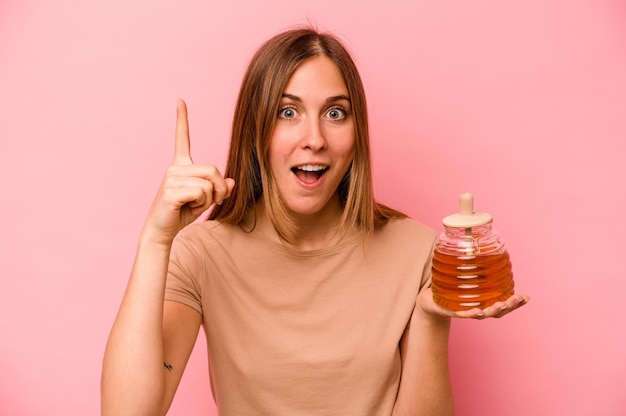 Junge kaukasische Frau, die Honig isoliert auf rosa Hintergrund hält und ein Ideeninspirationskonzept hat