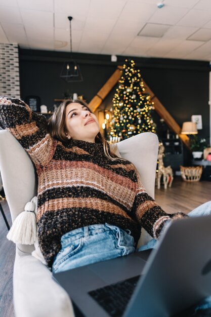 Junge kaukasische Frau, die im Sessel entspannt und Laptop-Computer in den Ferien zu Hause im Wohnzimmer verwendet.