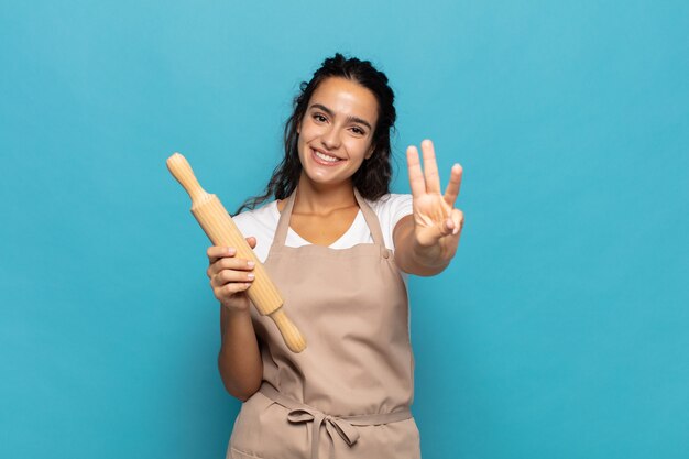 Junge kaukasische frau, die lächelt und freundlich schaut, nummer drei oder dritte mit hand nach vorne zeigend, countdown