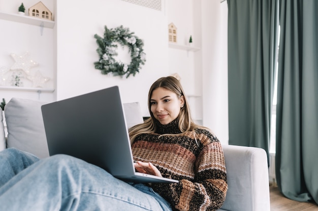 Junge kaukasische Frau, die Laptop-Computer in den Ferien zu Hause auf dem Sofa verwendet.