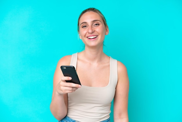 Junge kaukasische Frau, die mit einem Handy auf blauem Hintergrund isoliert ist