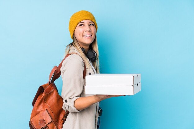 Junge kaukasische Frau, die Pizzas isoliert hält, schaut lächelnd, fröhlich und angenehm beiseite.