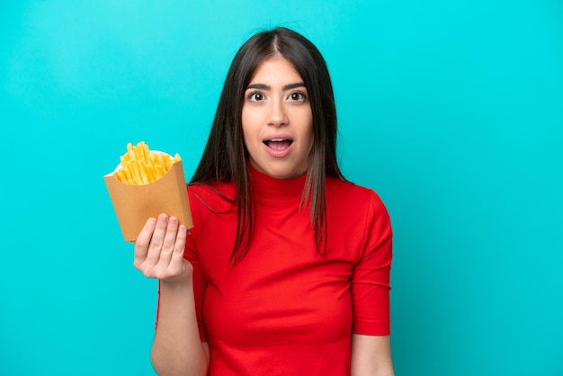 Junge kaukasische Frau, die Pommes frites fängt, isoliert auf blauem Hintergrund mit überraschendem Gesichtsausdruck