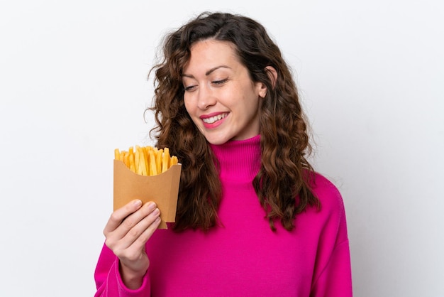 Junge kaukasische Frau, die Pommes-Frites lokalisiert auf weißem Hintergrund mit glücklichem Ausdruck fängt