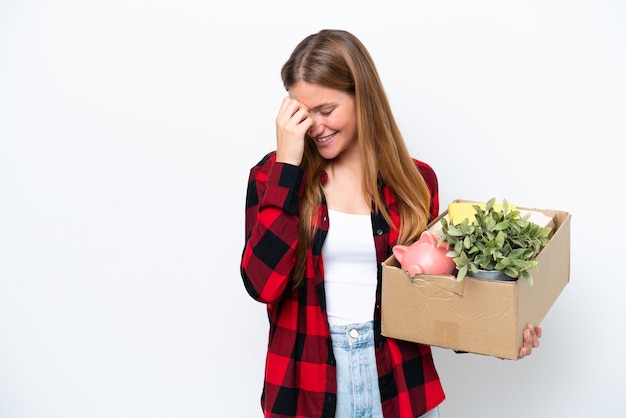 Junge kaukasische Frau, die sich bewegt, während sie eine Kiste voller Dinge aufhebt, die auf weißem Hintergrund lachen